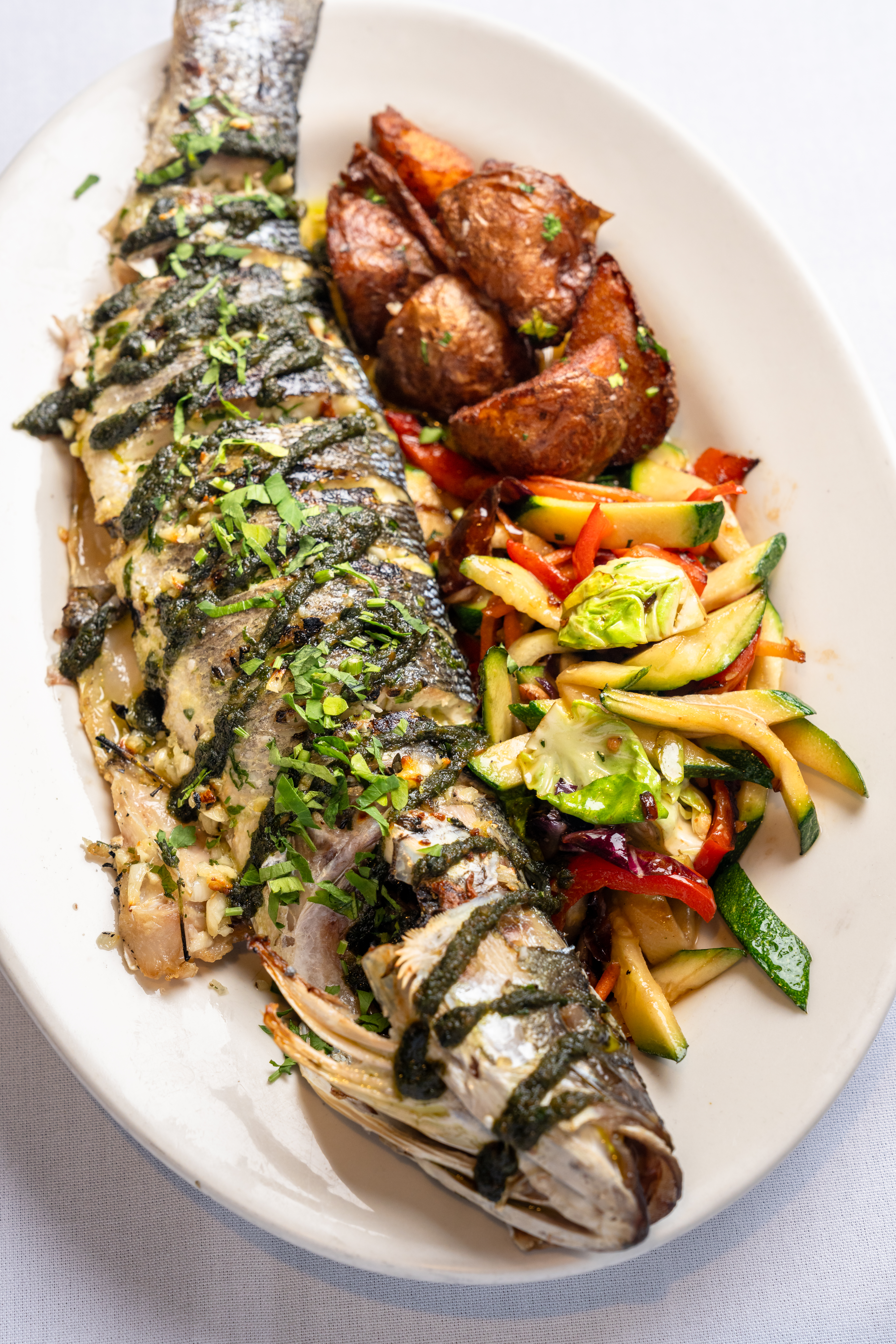 Whole-roasted Branzino with lemon and fresh herbs over a bed of vegetables.