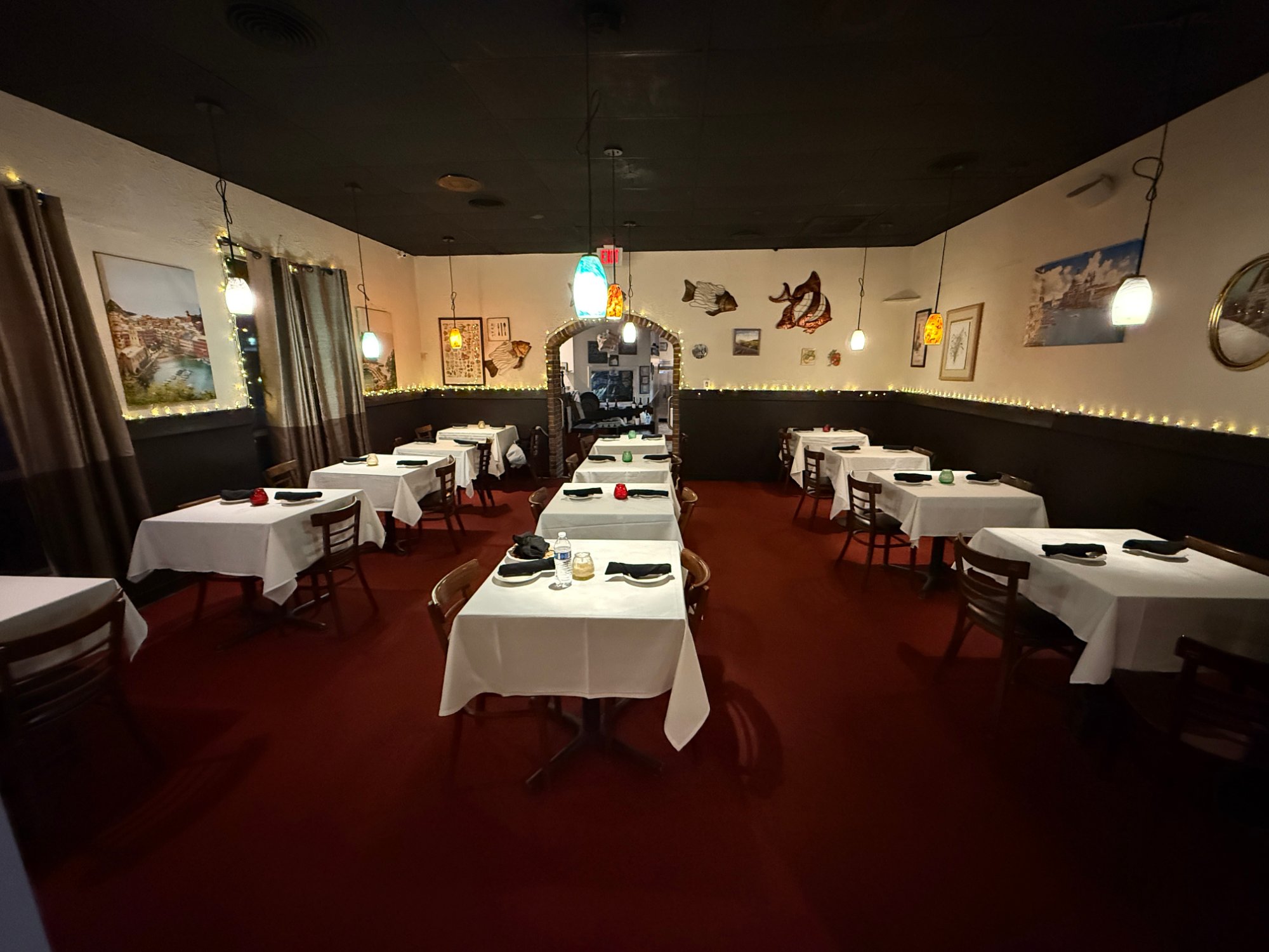 The warm Italian Trattoria-style dining room with white tablecloths and pendant lighting.